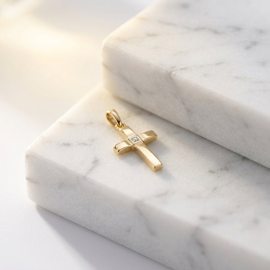 Goldener Kreuz-Anhänger mit Zirkonia in der Mitte auf weißen Marmorplatten, polierte Oberfläche in Gelbgold