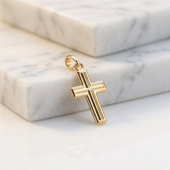Goldener Kreuz-Anhänger mit gerillter Oberfläche und Öse auf weißem Marmor