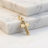 Goldener Kreuz-Anhänger mit gerillter Oberfläche und Öse auf weißem Marmor