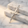 Silberner Kreuzanhänger mit detaillierter Christusfigur auf mattem Kreuz, ruhend auf weißen Marmorblöcken