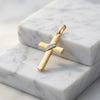 Goldener Kreuz-Anhänger mit diagonalem Band, polierte Oberfläche, auf weißem Marmor präsentiert