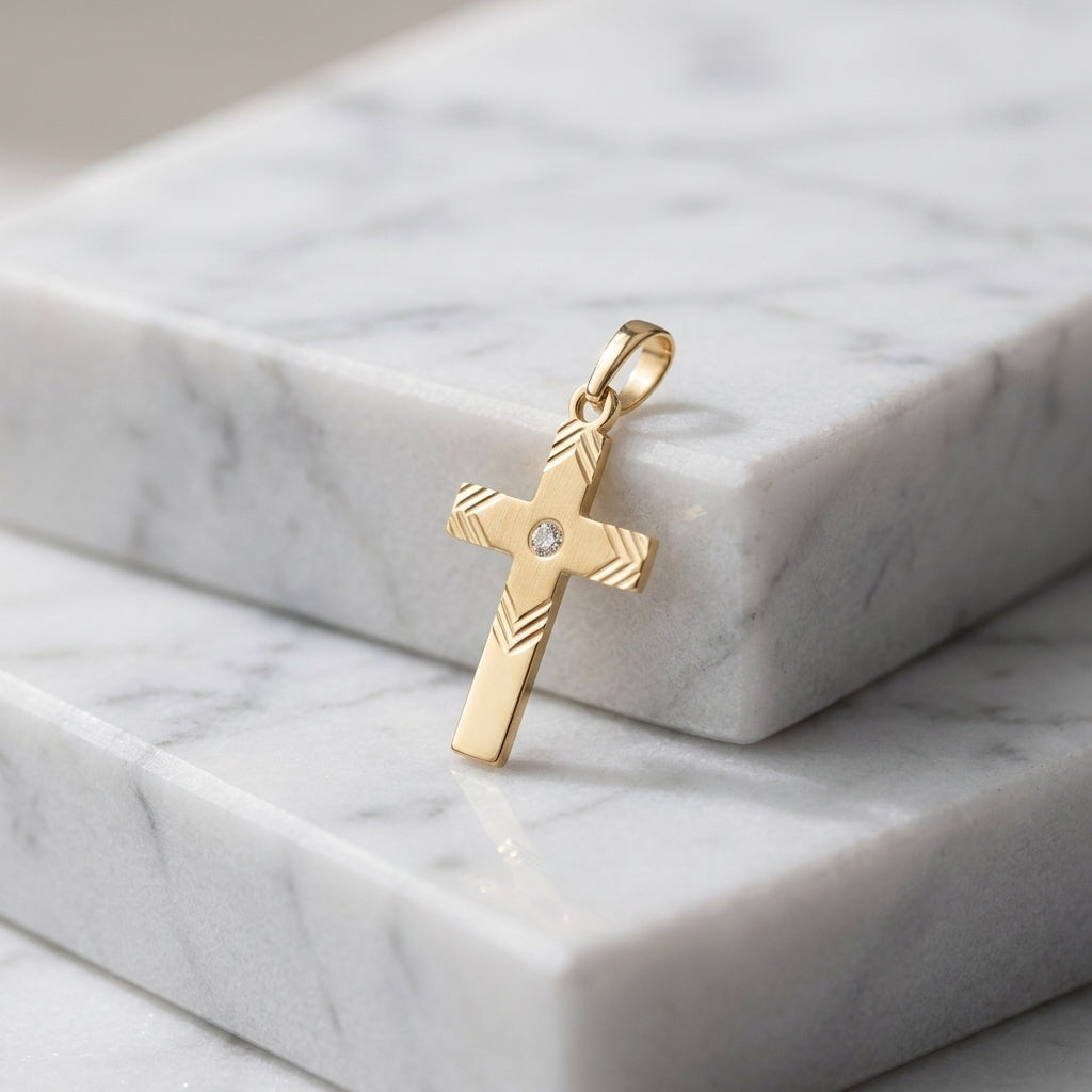 Goldener Kreuz-Anhänger mit Zirkonia und gefrästem Muster auf weißem Marmor