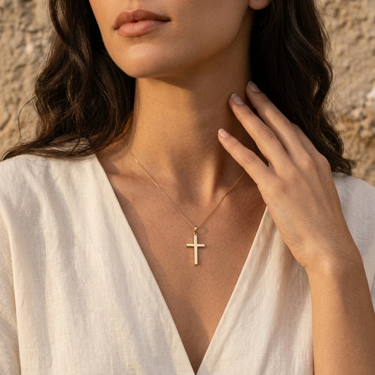 Frau trägt goldenen Kreuz-Anhänger Glory an filigraner Kette, weißes Leinenhemd, sonniges Ambiente