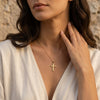 Frau trägt goldenen Kreuz-Anhänger Holy an filigraner Kette, weißes Leinenhemd, warmes Sonnenlicht