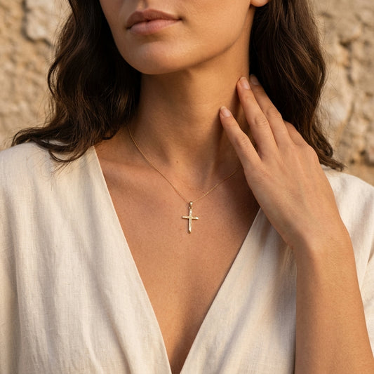 Frau trägt filigranen Kreuz-Anhänger Leaf aus Gold an zarter Kette, weißes Leinenhemd, natürlicher Look