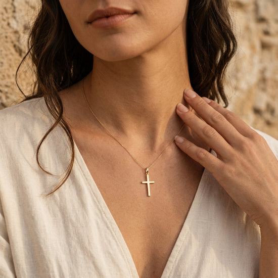 Frau trägt goldenen Kreuz-Anhänger Pure an filigraner Kette, minimalistisches Design aus Echtgold vor natürlichem Hintergrund