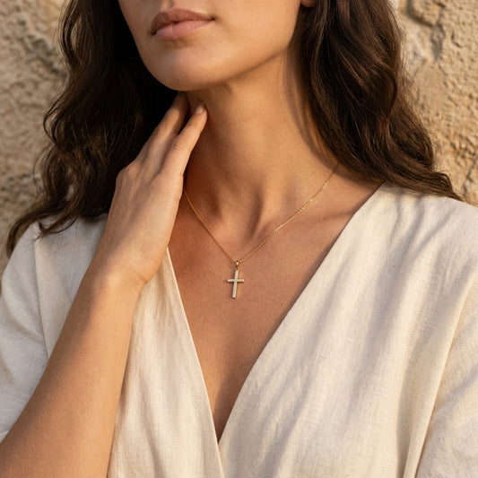 Frau trägt goldenen Kreuz-Anhänger Saviour an filigraner Kette, weißes Oberteil, Hand am Hals, warmes Sonnenlicht