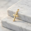 Goldener Kreuz-Anhänger Shine mit polierter Oberfläche und stilisiertem Design auf weißem Marmor