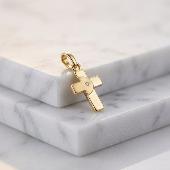 Goldener Kreuz-Anhänger mit funkelndem Zirkonia in der Mitte, auf weißem Marmor präsentiert