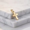 Goldener Kreuz-Anhänger mit funkelndem Zirkonia in der Mitte, auf weißem Marmor präsentiert