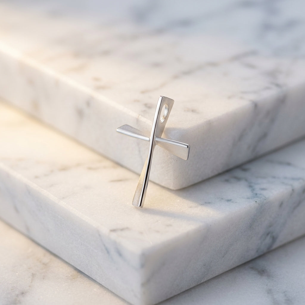Silberner Kreuz-Anhänger mit gedrehtem Design auf weißen Marmorblöcken, polierte Oberfläche reflektiert sanft das Licht