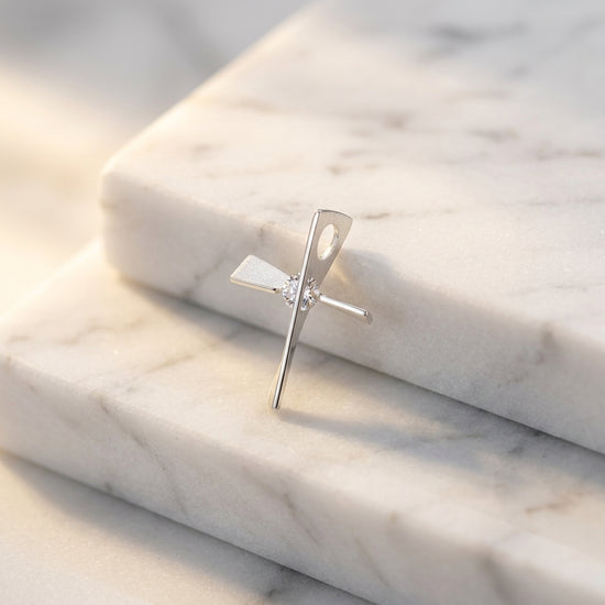 Silberner Kreuz-Anhänger mit gedrehtem Design und funkelndem Zirkonia-Stein auf weißem Marmor