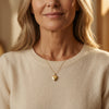 Goldenes Herz-Medaillon Pure Grand an filigraner Kette, getragen von Frau in beigem Pullover