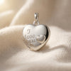 Silbernes Herz-Medaillon mit Gravur "I love you" und kleinem Herz, aufklappbar, auf cremefarbenem Seidenstoff