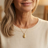 Goldenes Oval-Medaillon mit graviertem Ornament an feiner Kette, getragen am Hals einer Frau in beigem Pullover