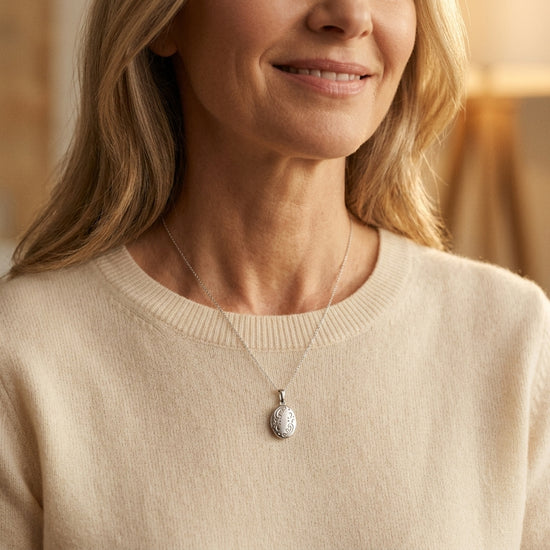 Frau trägt silbernes Oval-Medaillon Iris mit filigranem Muster an zarter Kette über beigem Pullover