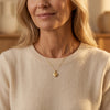 Goldenes Herz-Medaillon Laurel an filigraner Kette, getragen von Frau in cremefarbenem Pullover