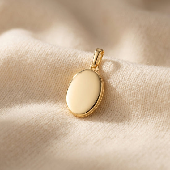 Goldenes Oval-Medaillon auf cremefarbenem Stoff, polierte Oberfläche mit zarter Kette-Öse, Aurevia Manufaktur