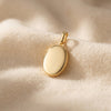 Goldenes Oval-Medaillon auf cremefarbenem Stoff, polierte Oberfläche mit zarter Kette-Öse, Aurevia Manufaktur