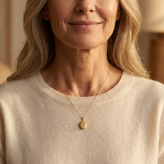 Frau trägt goldenes Oval-Medaillon Pure Petite an feiner Kette über beigem Pullover, dezent glänzend