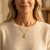 Frau trägt goldenes Oval-Medaillon mit Pfingstrosen-Gravur an filigraner Kette, cremefarbener Pullover