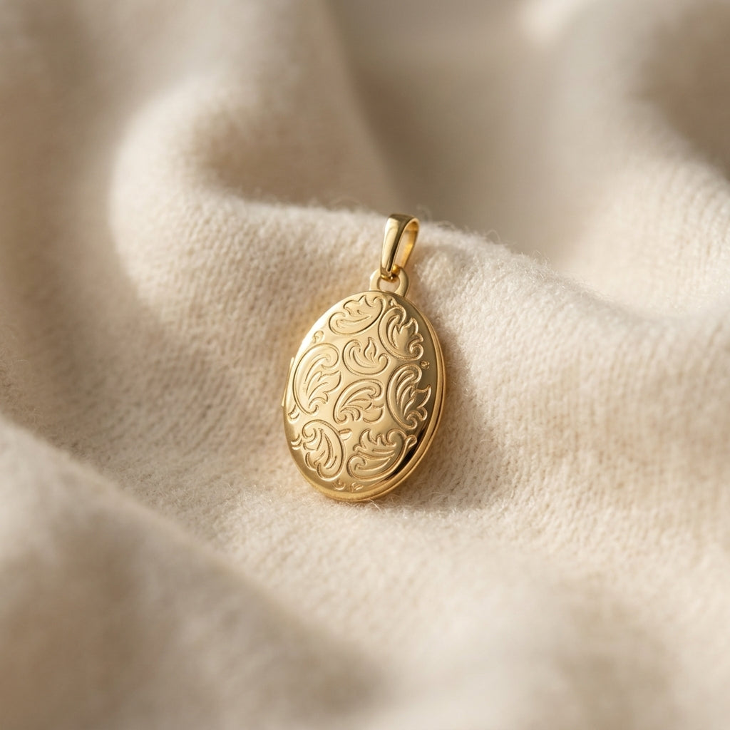Gold-Medaillon mit floraler Gravur auf cremefarbenem Stoff, ovale Form mit feinem Schnörkeldekor, Anhänger mit Öse
