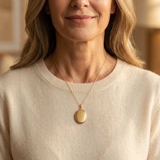 Frau trägt goldenes Oval-Medaillon Pure Grand an feiner Kette, polierte Oberfläche, zeitlos elegant über cremefarbenem Pullov