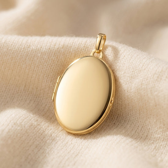 Goldenes Oval-Medaillon Pure Grand zum Öffnen auf cremefarbenem Stoff, polierte Oberfläche, mit Aufhängeöse