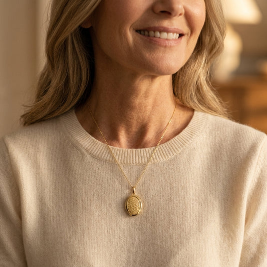 Goldenes Oval-Medaillon mit geometrischem Muster an feiner Kette, getragen von Frau in beigem Pullover