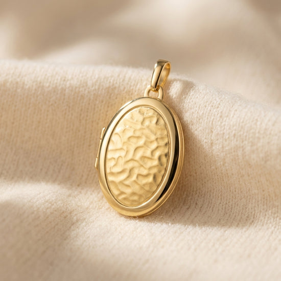 Goldenes Oval-Medaillon mit gehämmerter Oberfläche auf cremefarbenem Stoff, aufklappbar, hochglanzpolierter Rand