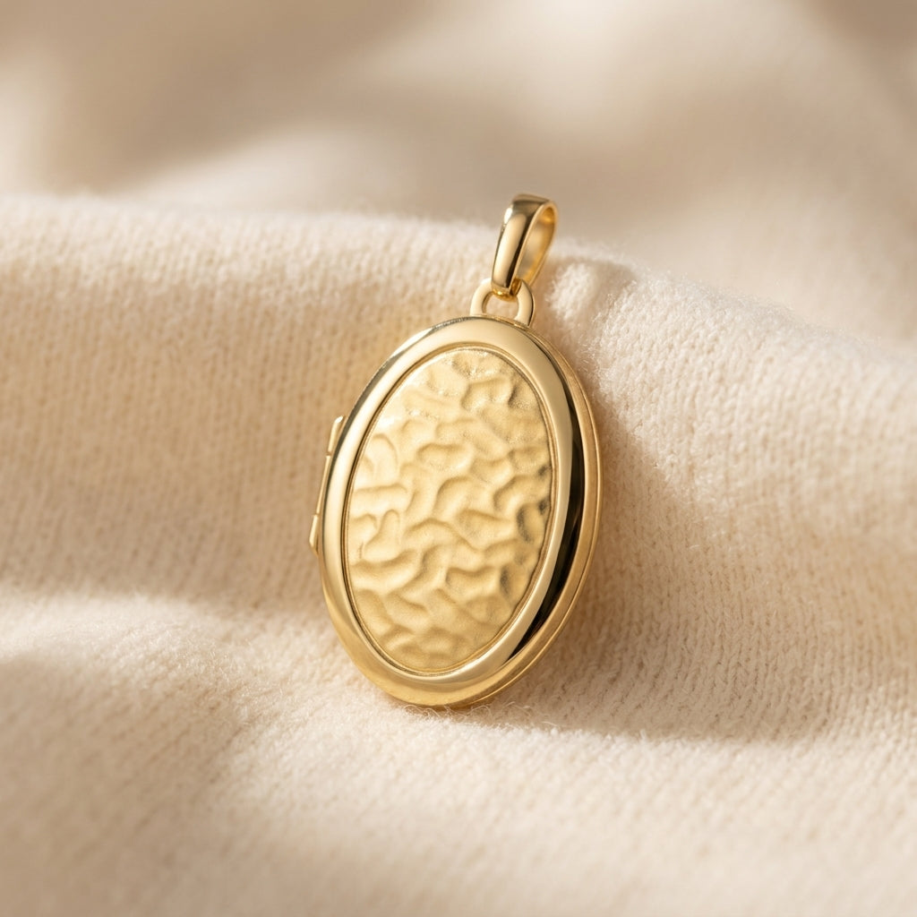 Goldenes Oval-Medaillon mit gehämmerter Oberfläche auf cremefarbenem Stoff, aufklappbar, hochglanzpolierter Rand