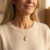 Goldenes Medaillon mit Stern-Gravur und Brillant an filigraner Kette, getragen von Frau in hellem Pullover