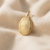 Goldenes Oval-Medaillon mit gravierter Oberfläche und ornamentaler Umrandung auf cremefarbenem Seidenstoff
